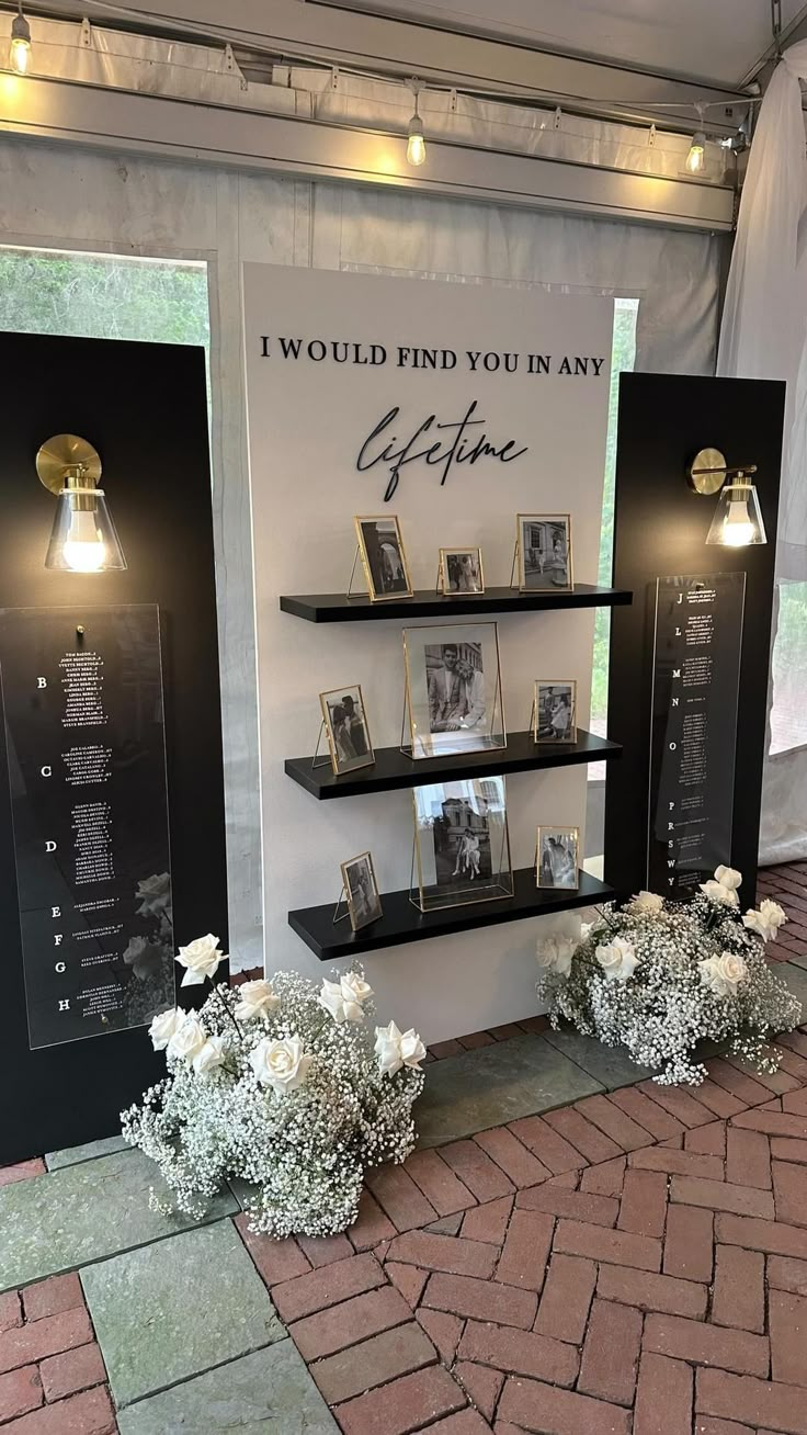 the display is decorated with white flowers and framed pictures on black shelves, along with small vases filled with baby's breath