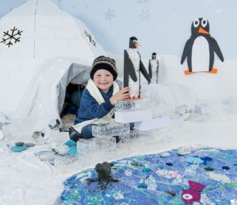 a little boy sitting in front of an igloose with penguins on it