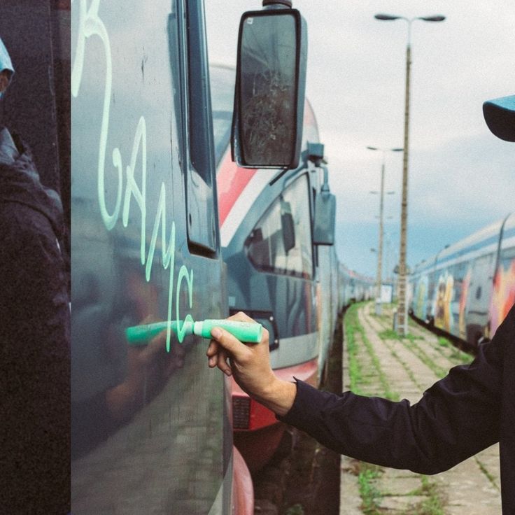 a man writing on the side of a train next to another person wearing a hat