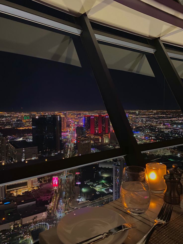 a table with plates and silverware is overlooking the city lights from a high rise restaurant