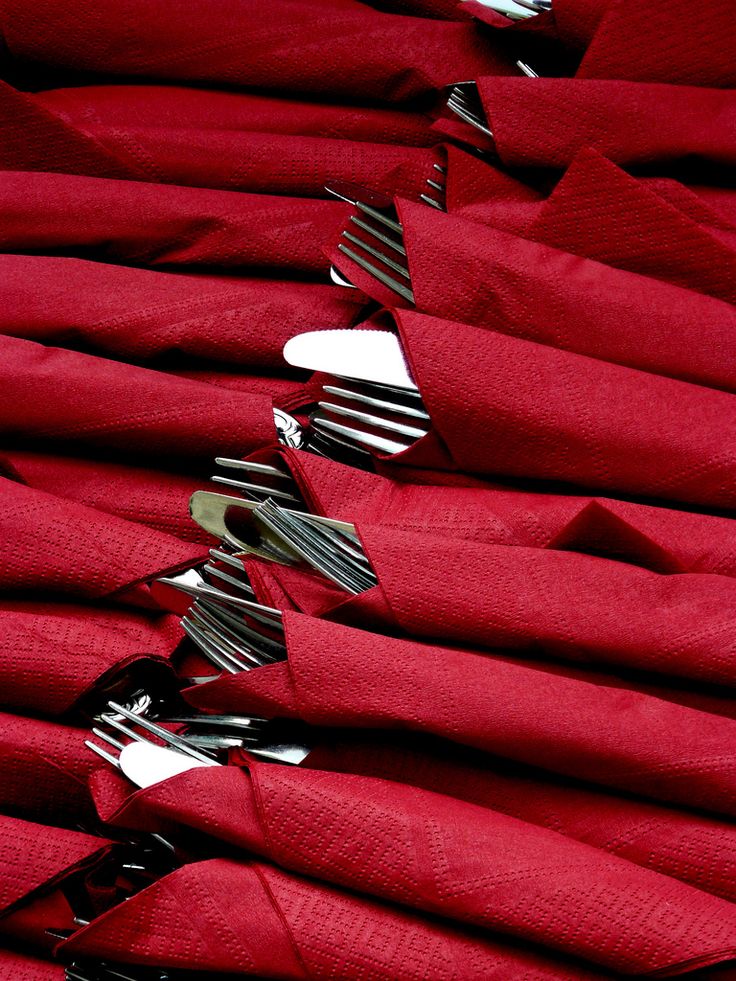 forks and spoons are placed in the middle of folded red napkins on top of each other