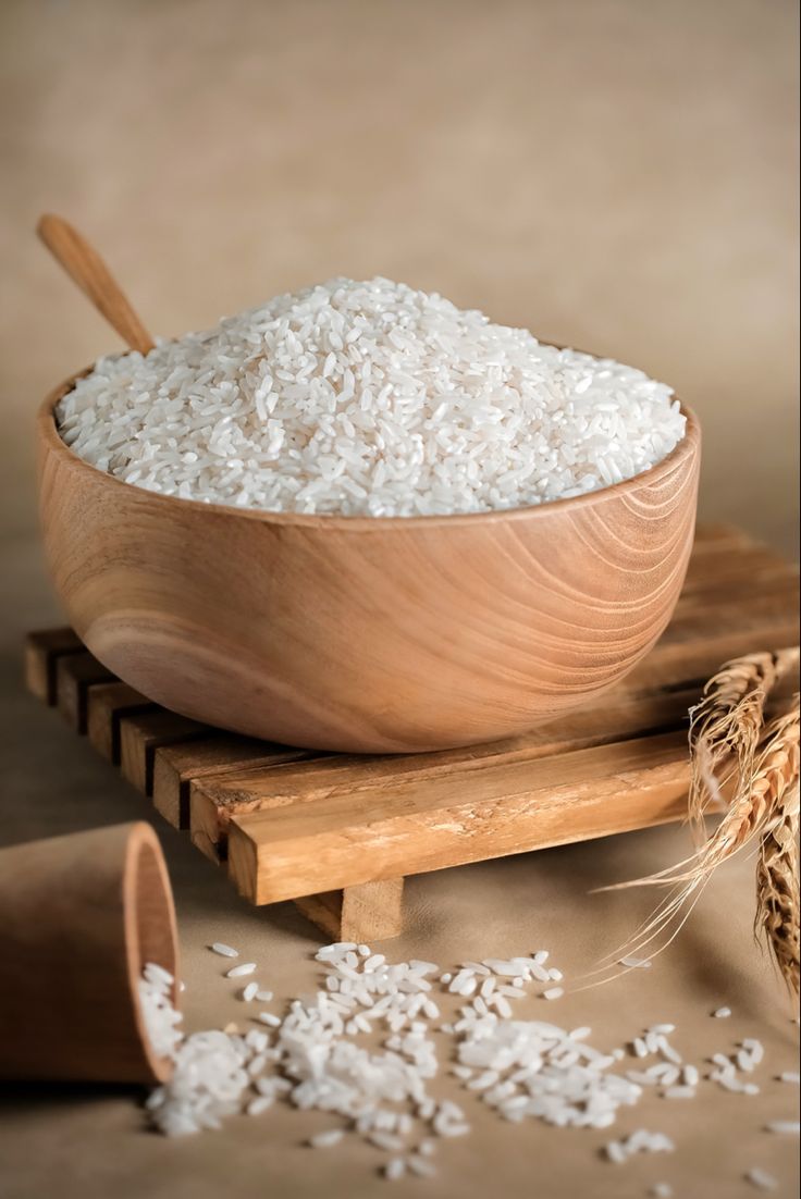 a wooden bowl filled with rice on top of a cutting board next to an ear of wheat