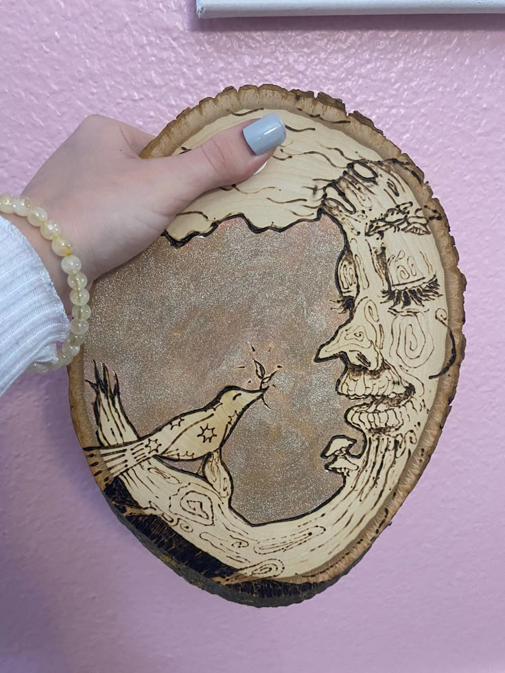 a woman's hand holding a wooden plaque with a drawing of a bird on it