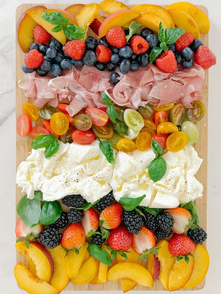 an assortment of fruits and meats arranged on a cutting board for a platter