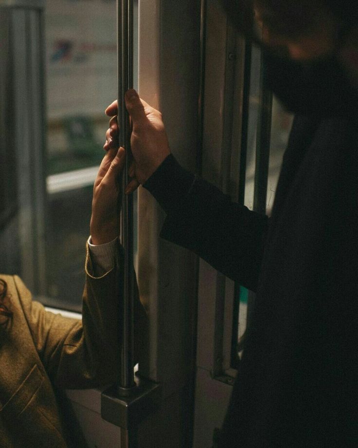 a man is holding onto the handle of a door on a subway car while another person looks at him