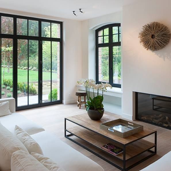 a living room filled with furniture and a fire place in front of two large windows