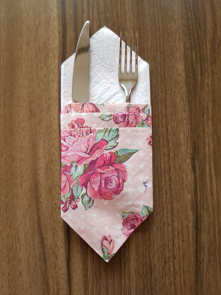 a fork and napkin on top of a wooden table with a pink flowered design