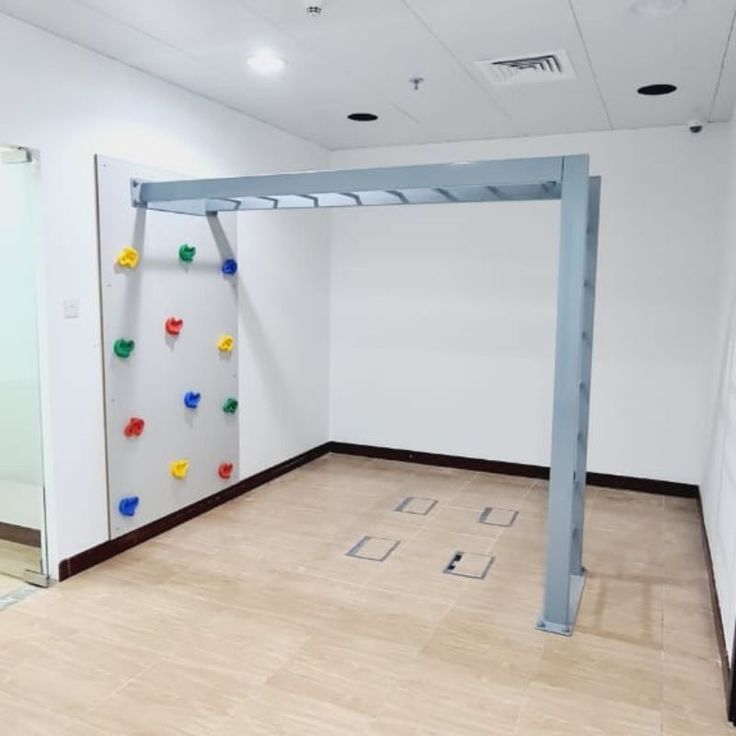 an empty room with white walls and wooden flooring has climbing equipment on the wall