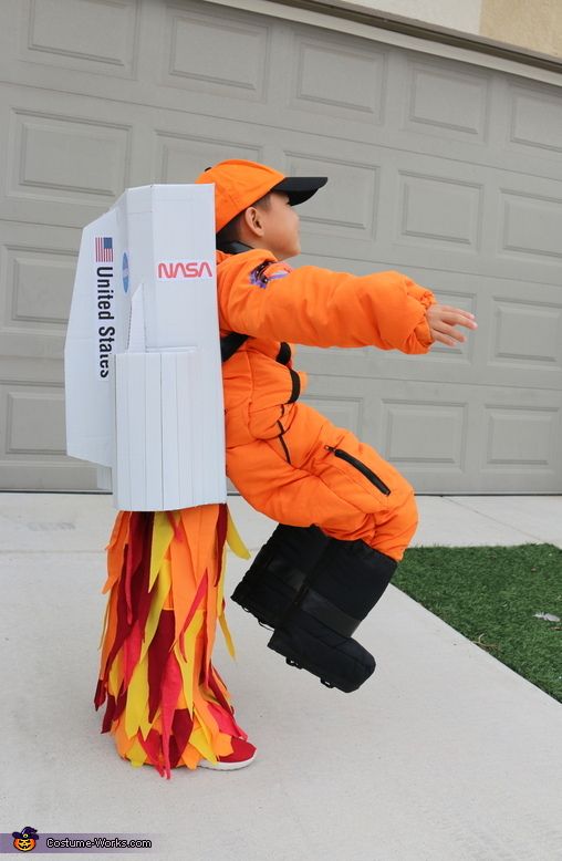 a young boy dressed in an orange costume is playing with a cardboard box on the sidewalk