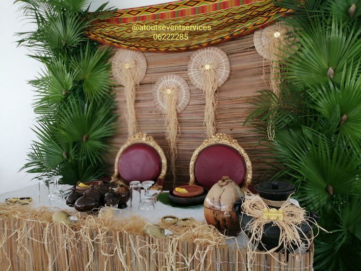 a table topped with plates and bowls next to palm trees in front of a wall