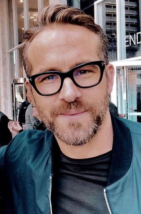 a man with glasses and a beard is posing for the camera in front of a building