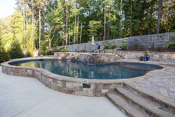 a pool with steps leading up to it in the middle of a patio and landscaping area