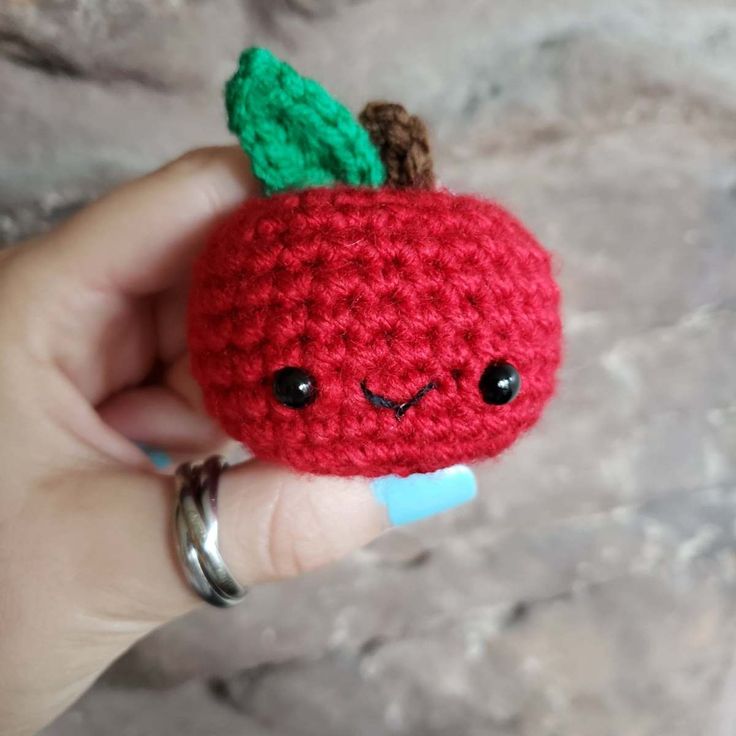 a crocheted red apple with a green leaf on it's head and eyes