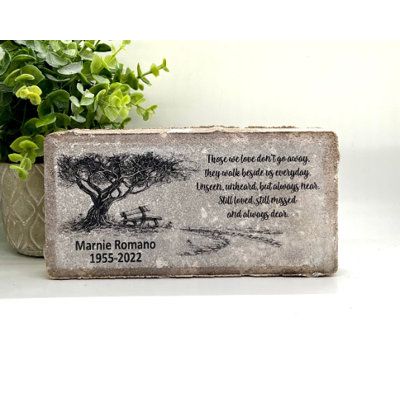 a memorial stone with a tree and bench in the background next to a potted plant