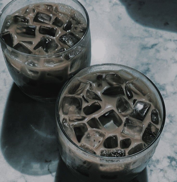 two glasses filled with ice sitting on top of a marble counter next to each other