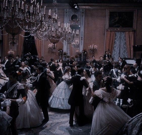 a group of people dressed in formal wear dance together with chandeliers hanging from the ceiling