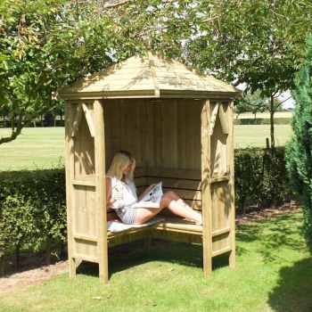 a woman sitting in a wooden gazebo reading a book on the grass next to some trees