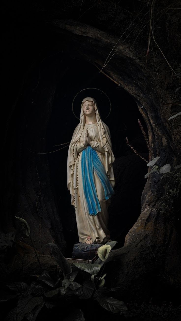 the virgin mary statue is standing in front of a dark tunnel with leaves on it