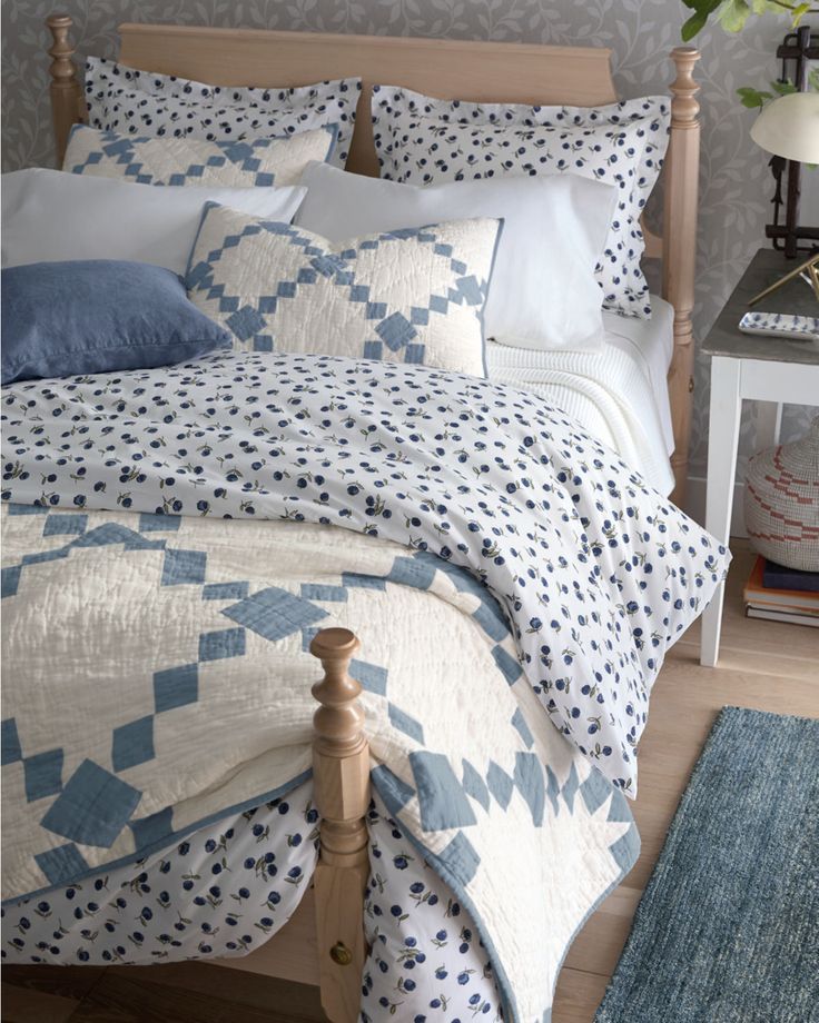 a bed with blue and white quilts on top of it next to a night stand