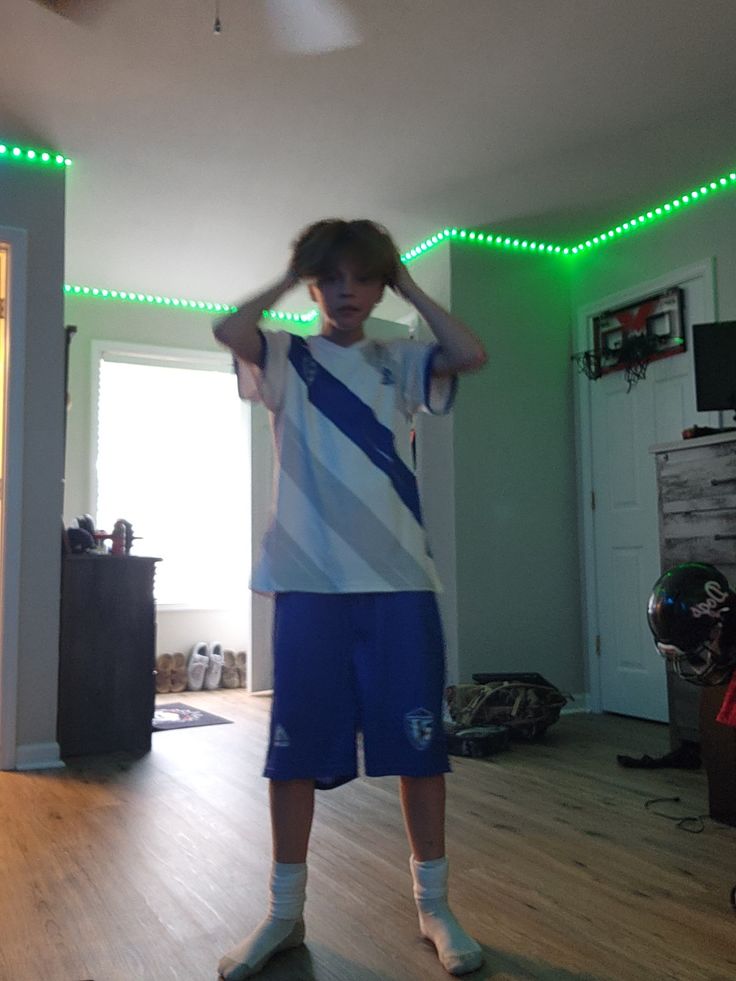 a young boy standing in a living room holding his hands to his head while wearing blue and white shorts