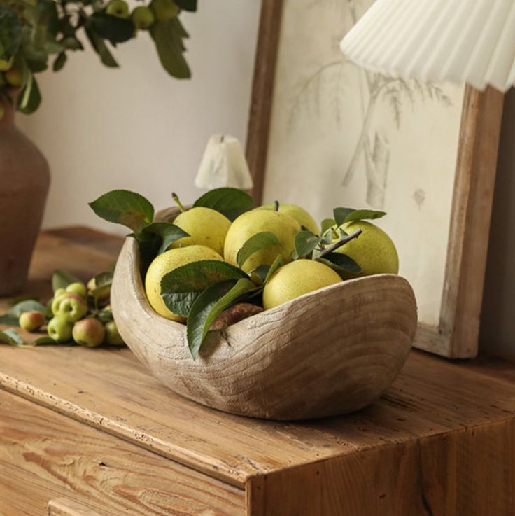 a wooden bowl filled with green apples on top of a table next to a lamp