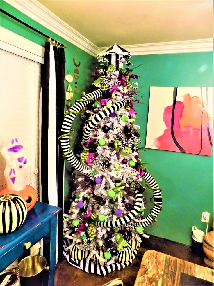 a christmas tree decorated with black and white striped ornaments in a living room area next to a painting on the wall