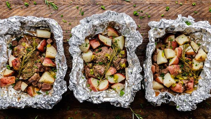 three tin foil trays filled with food on top of a wooden table next to each other