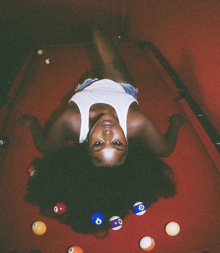 a woman laying on top of a pool table surrounded by billiards and balls