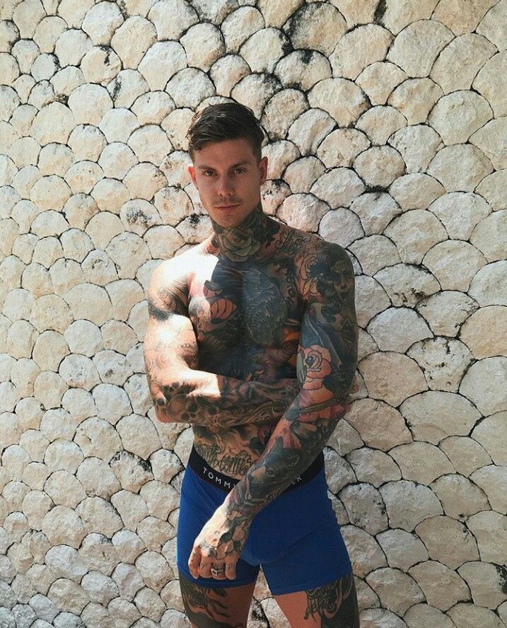 a man with tattoos standing in front of a stone wall