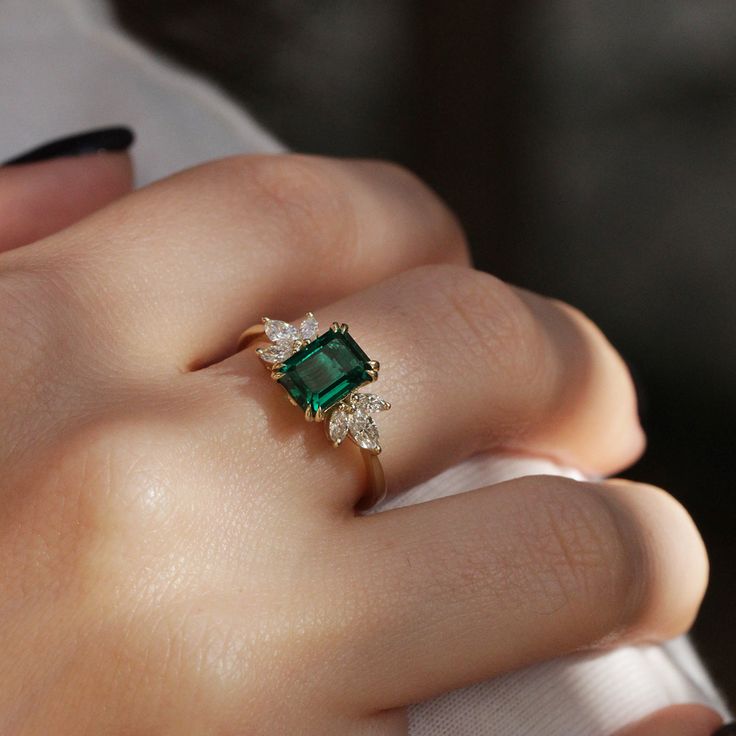 a close up of a person's hand wearing a ring with an emerald and diamond