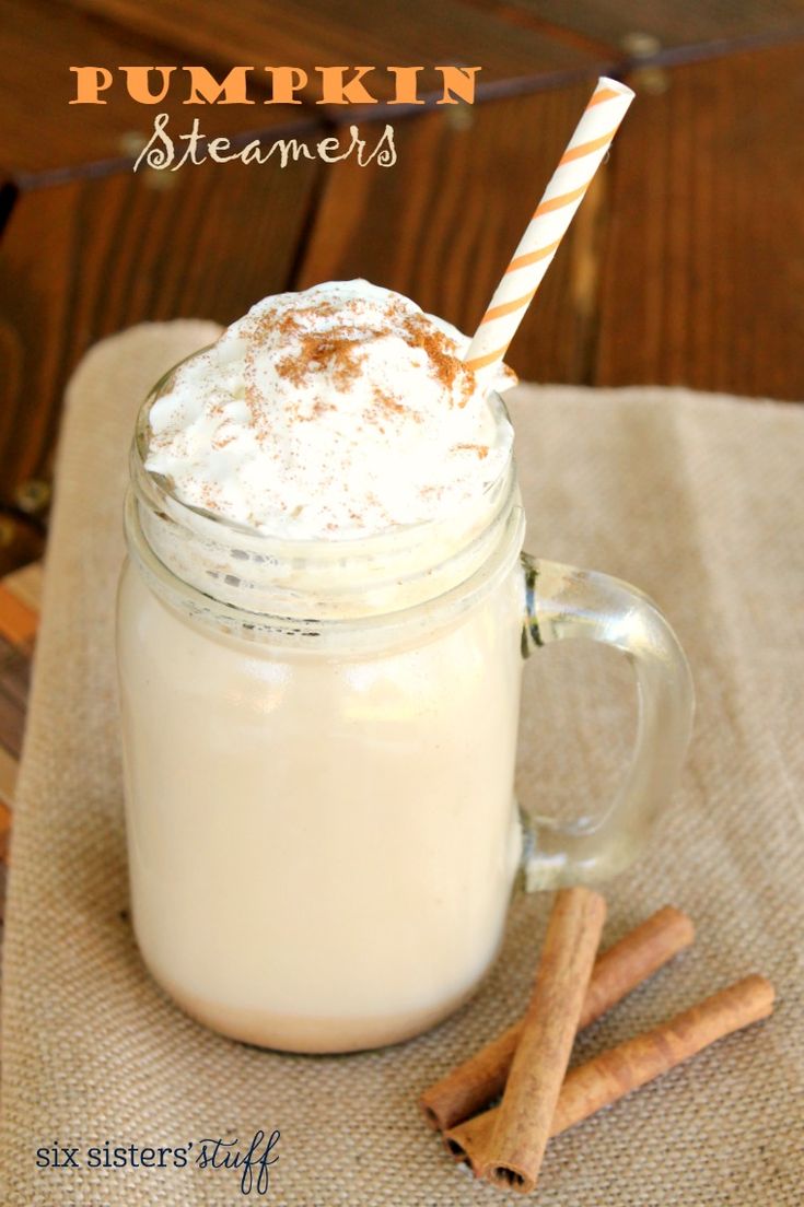 a glass mug filled with whipped cream and cinnamon sticks on top of a tablecloth