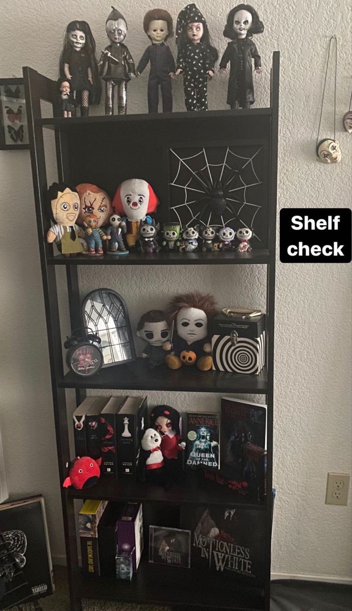 a shelf filled with lots of creepy dolls and other halloween related items in front of a white wall