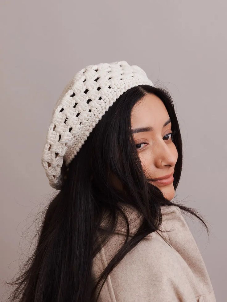 a woman with long hair wearing a white crochet beanie and smiling at the camera