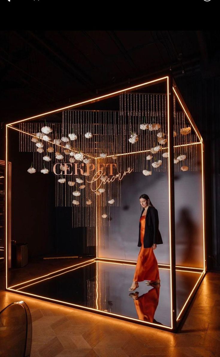 a woman standing in front of a mirror with lights hanging from the ceiling and chandelier