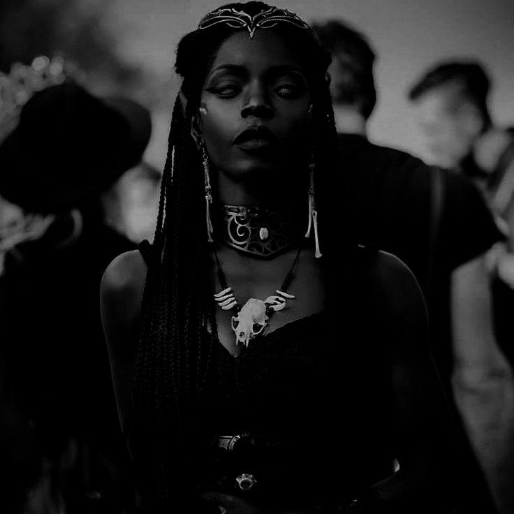 a woman with long braids standing in front of a group of people wearing black clothing