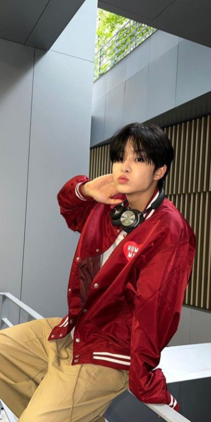 a young man sitting on top of a metal rail wearing a red jacket and khaki pants