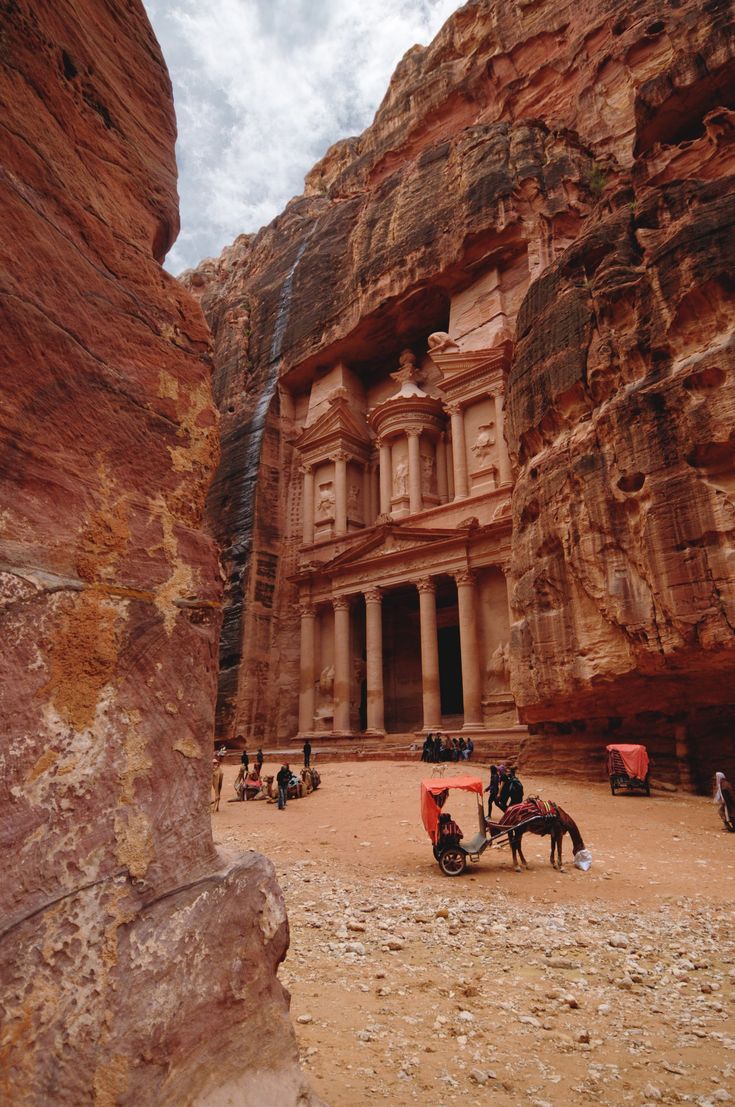 some people and horses in front of a large rock building with two storyed buildings