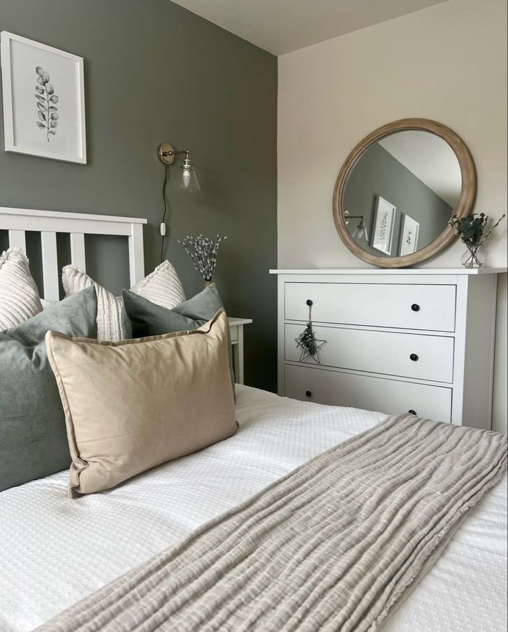 a white bed sitting next to a dresser with a mirror on it's side