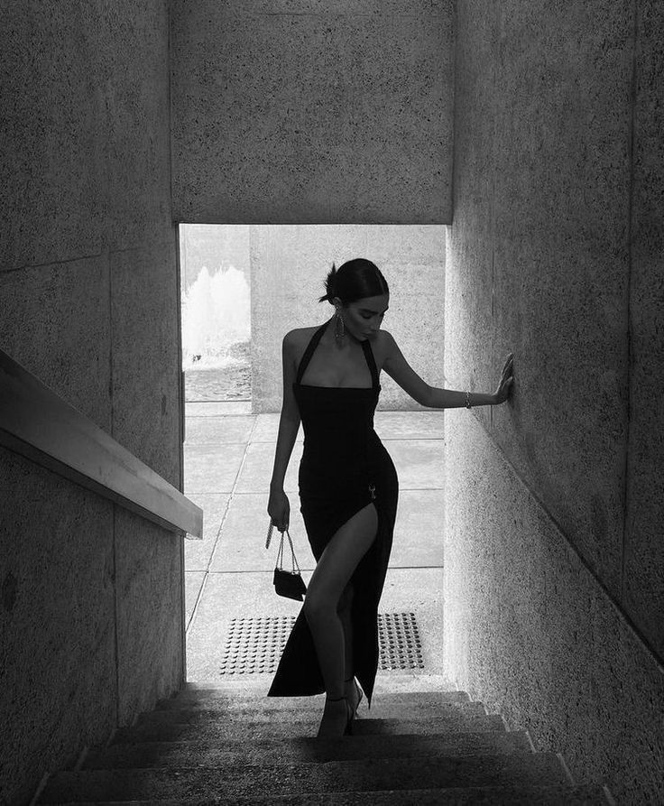 a woman in a black dress is walking up some stairs with her hand on the wall