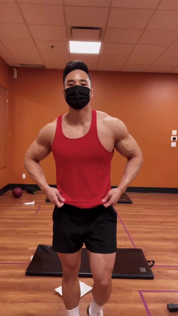 a man in a red tank top and black shorts wearing a face mask while standing on a yoga mat