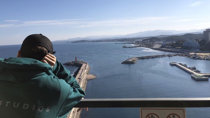 a man in a green hoodie is looking out over the water from a balcony