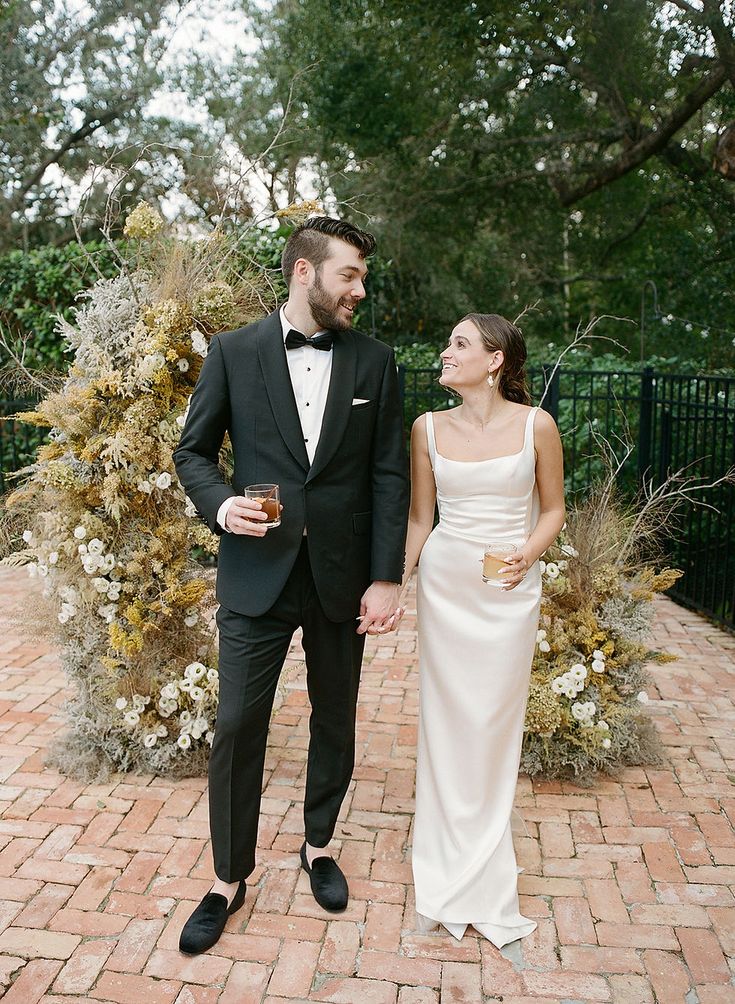 a man in a tuxedo and a woman in a white dress holding hands