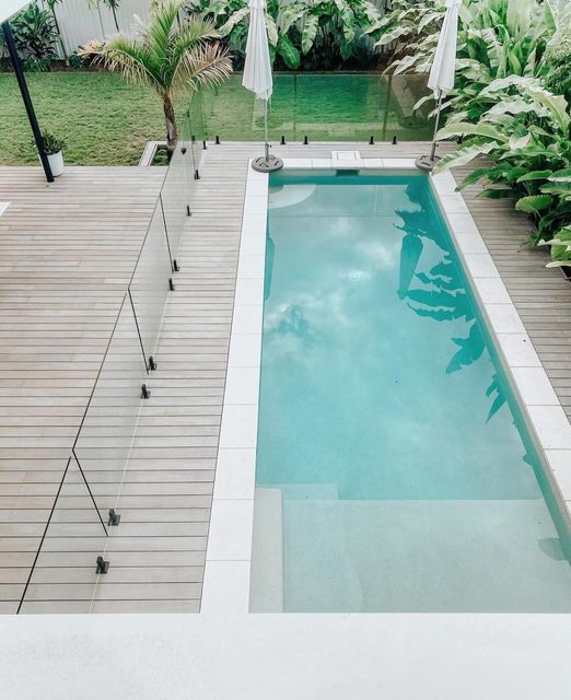 an empty swimming pool surrounded by greenery and umbrellas on the decking area