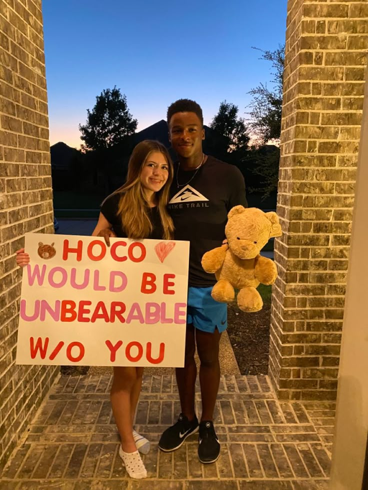 a man and woman standing next to each other holding a sign that says hoco would be unbearable two you