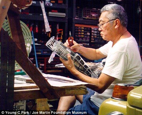 an older man sitting at a table working on a piece of art in his workshop