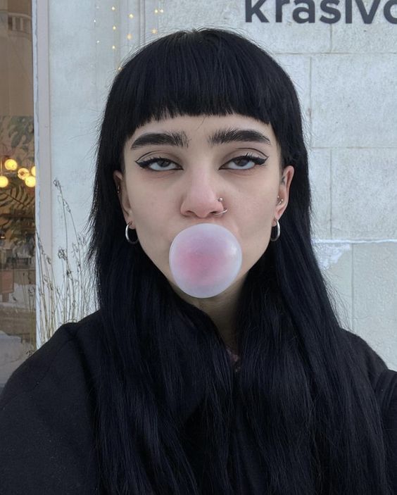 a woman with long black hair blowing a bubble