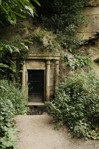 an entrance to a cave in the side of a mountain with plants growing around it