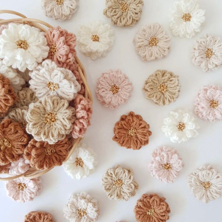 several crocheted flowers in a basket on a white surface next to other crocheted flowers