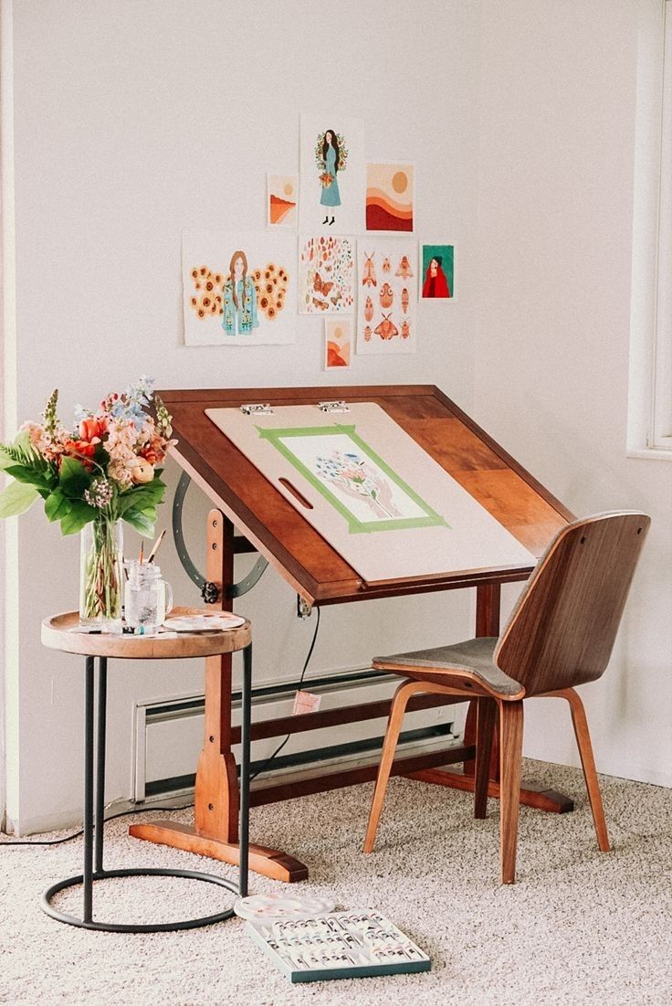 a small table and chair in front of a wall with pictures on it next to a window