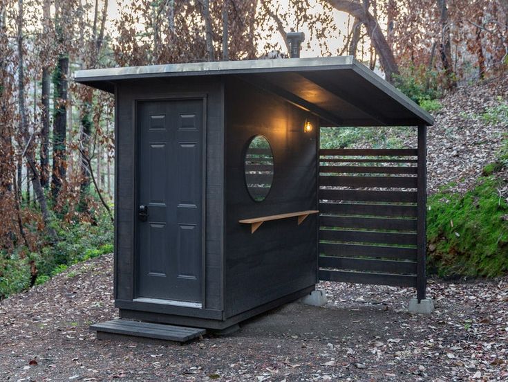 a small black outhouse in the woods